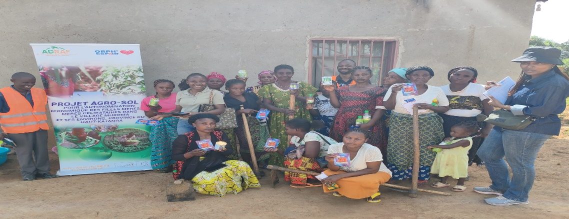 Groupe de bénéficiaires tenant les semences et boutures reçues devant la banderole du projet Agro-Sol